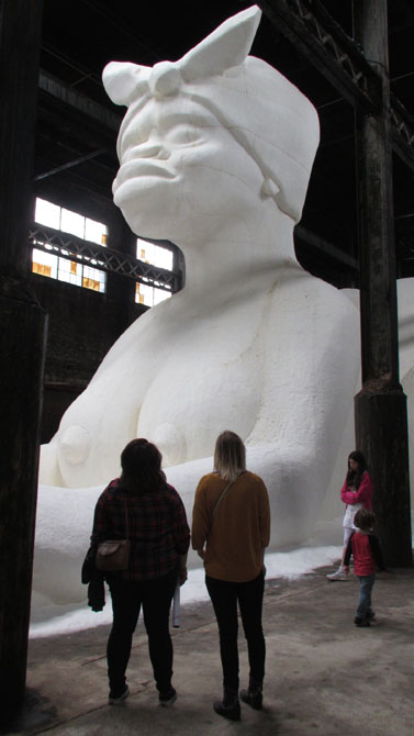 Dark figures in front of large white sculpture in museum setting