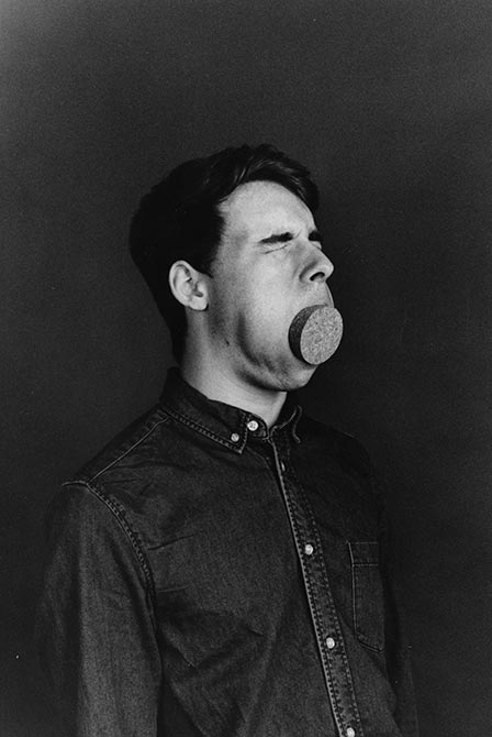 Young man with large cork in mouth, eyes shut.lsu intermediate photography