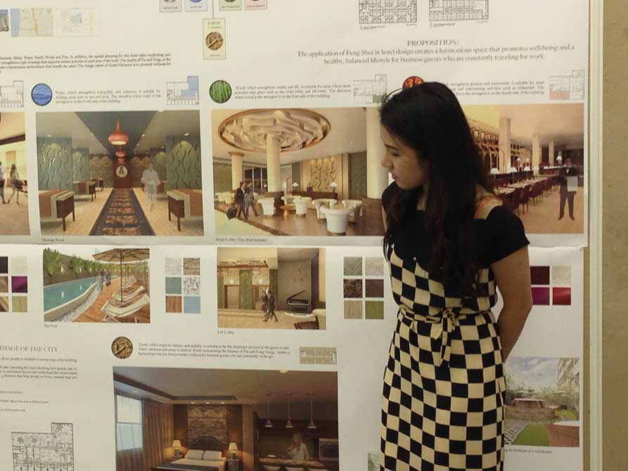 Young woman in checkered dress presents work.lsu interior design student work