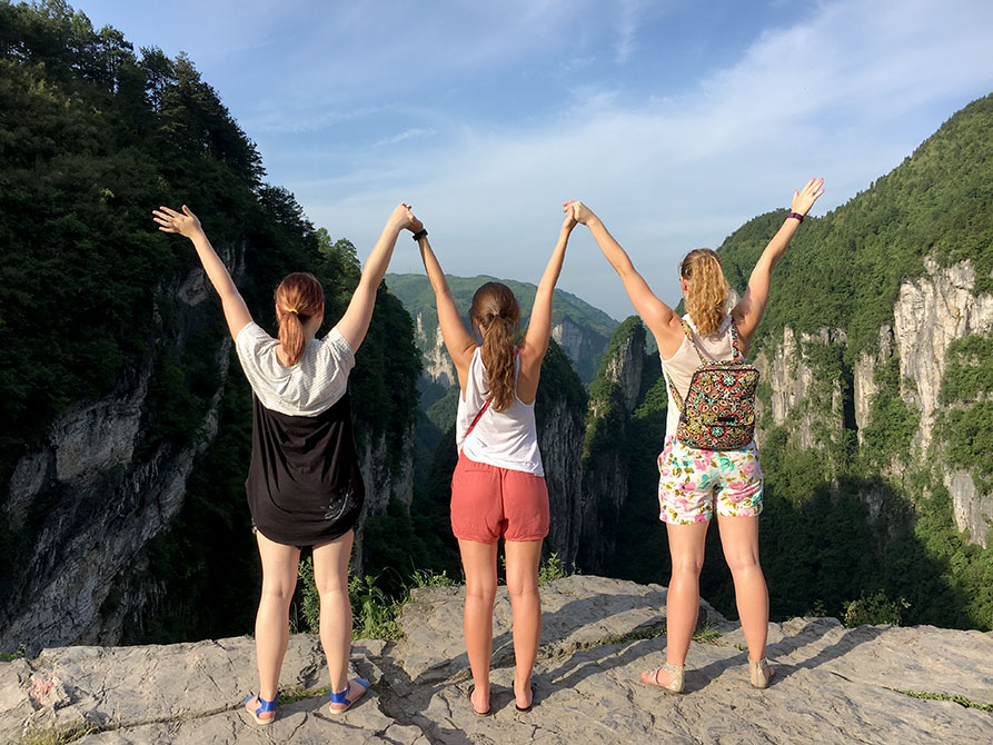 Girls raise arms in front of cliffs