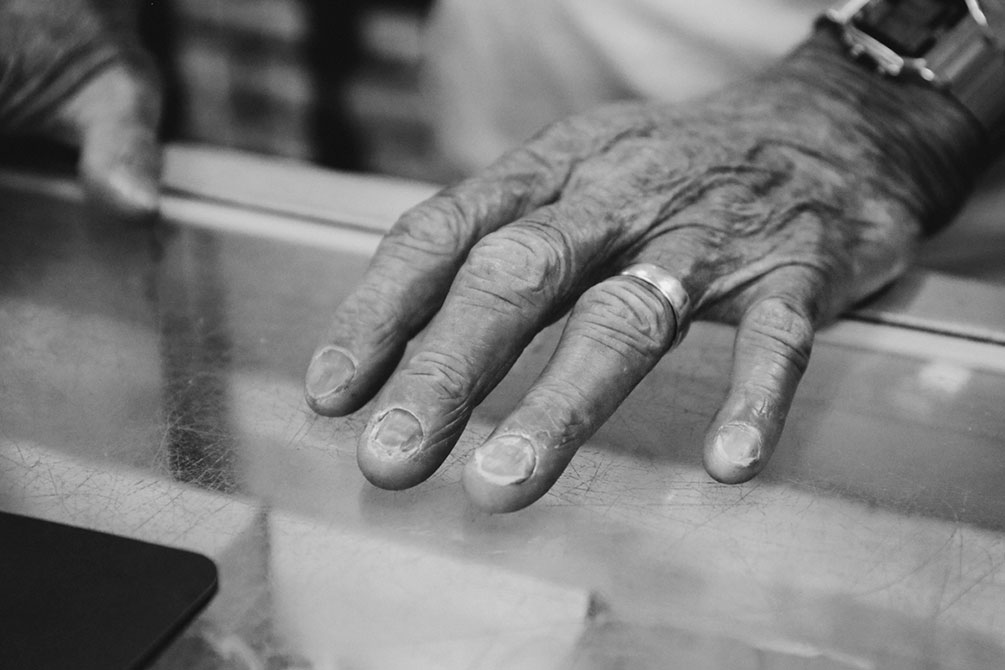 An old wrinkled hand rests on a table