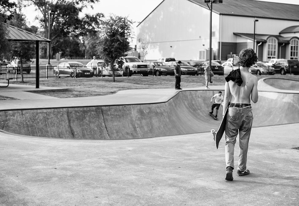 Man with shirt off walks in skate park