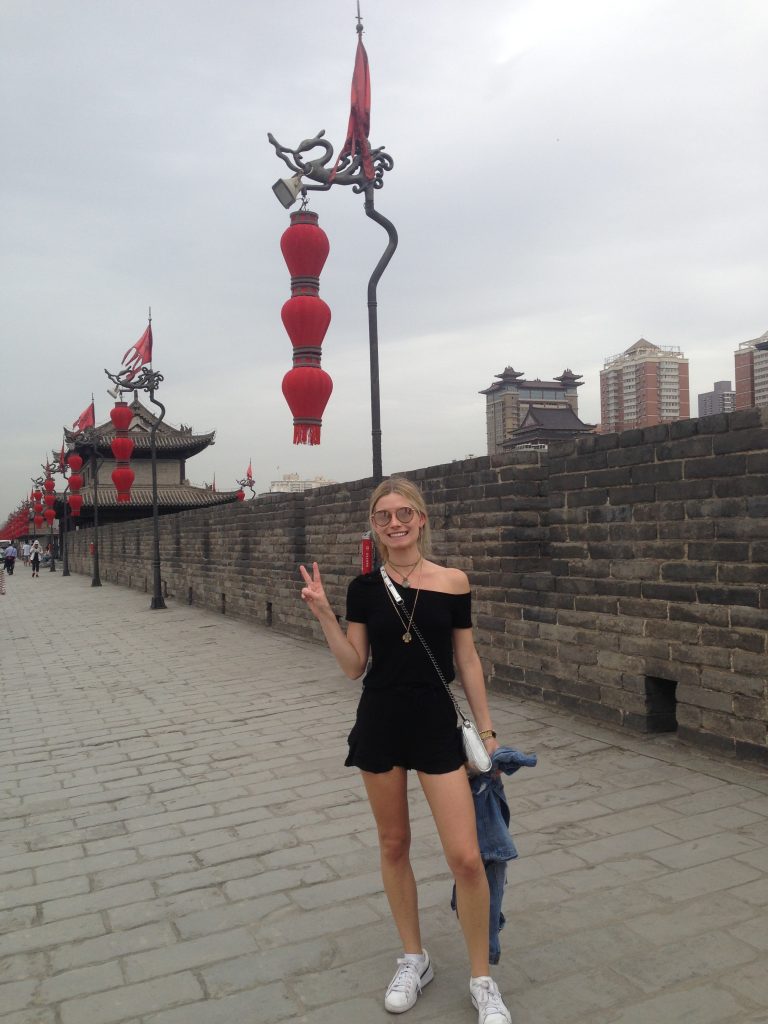 Student waving to camera in front of red chinese lanterns in street