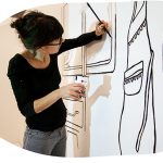 Paula Troxler paints an image with black lines on a white wall