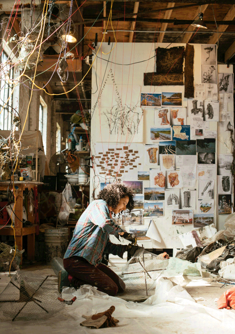 Hannah Chalew kneels while working in a crowded studio