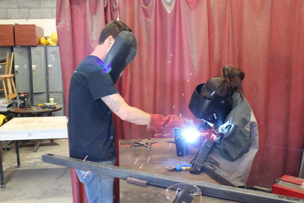 Two students with masks welding in shop