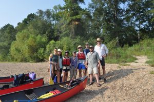 Group on sandy river back by red canoes