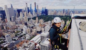 Elyse Marks scales skyscraper with view of New York City in background.