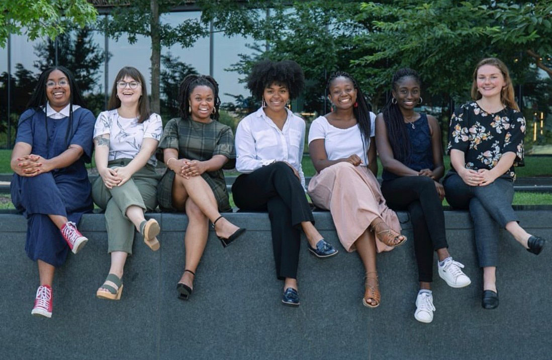 Row of young women sitting on wall, legs crossed