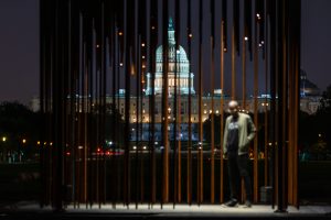 View of Capitol building in Washington, DC.illuminated at night, through bars.Black man stands in cage.