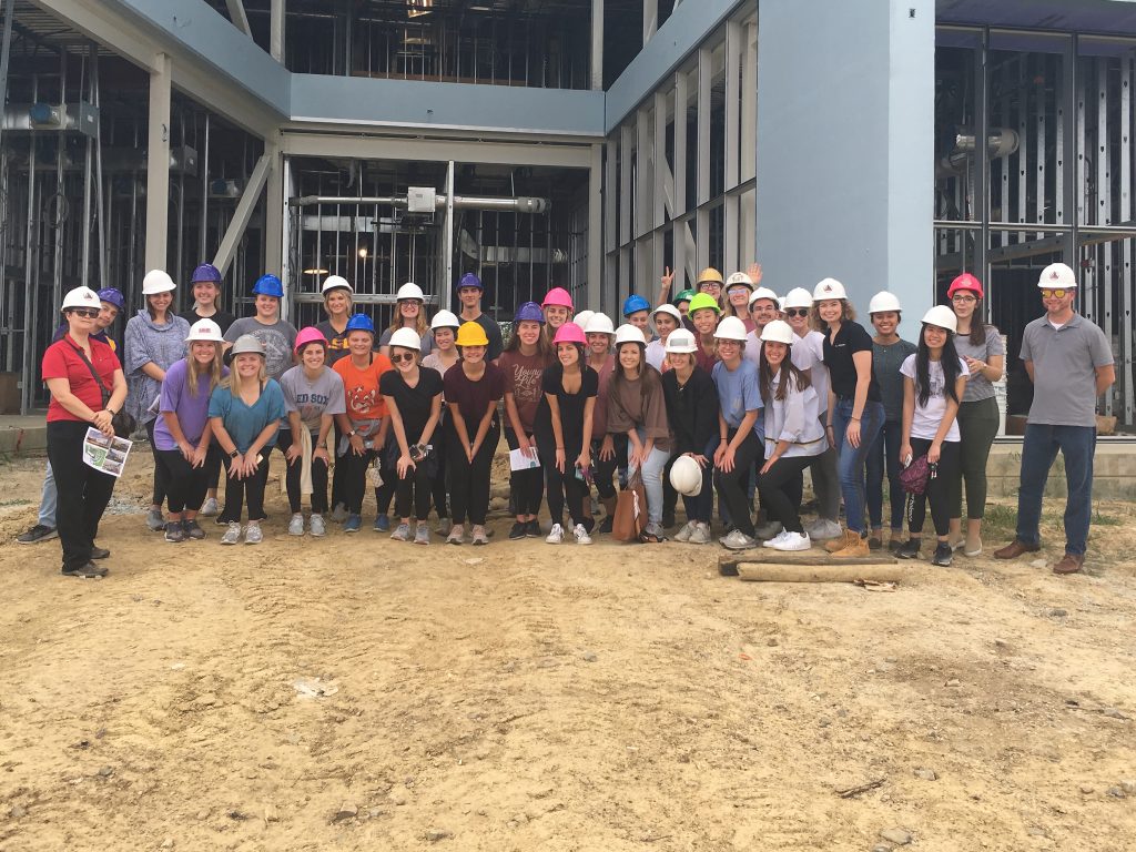 Group of students wearing hardhats in front of construction site.