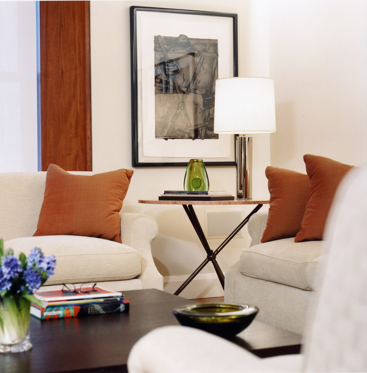 Living room with cream furniture, burnt orange pillows, vase of blue flowers on table, framed art on wall