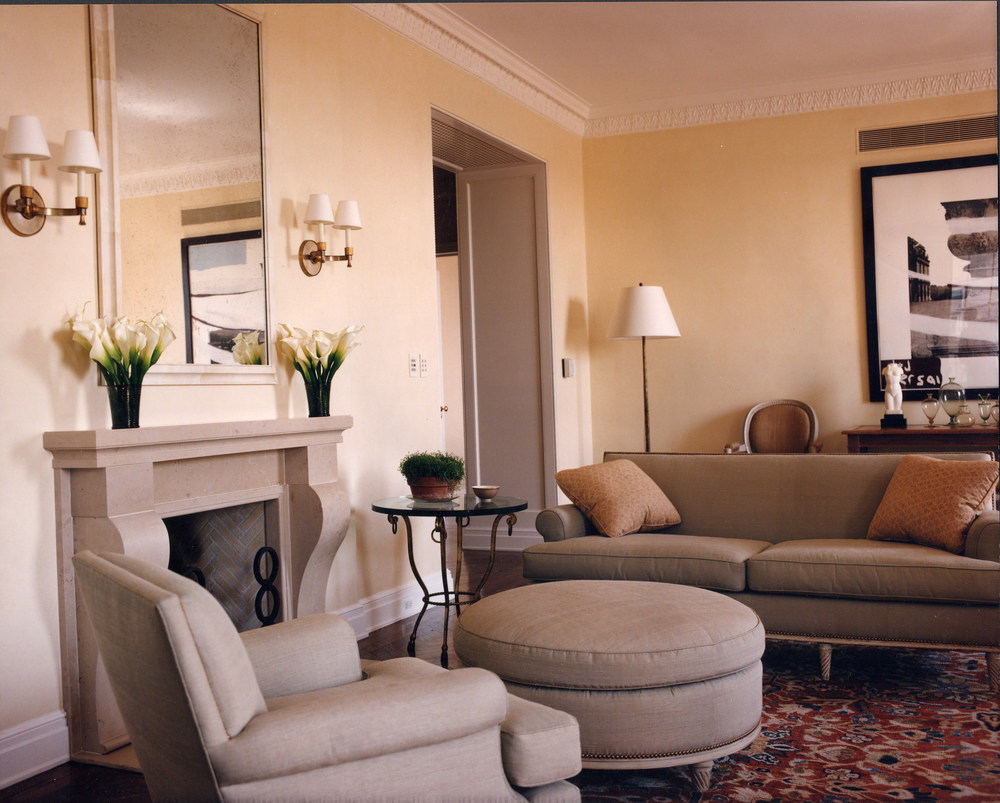 Room with gray furniture, beige walls, large mirror over fireplace, tulips in vases on mantle