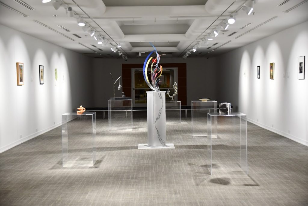 sculptures on clear glass podiums in well-lit gallery