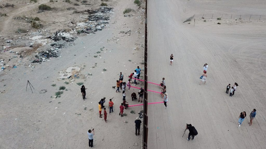 people on opposite sides of wall connected by pink rope